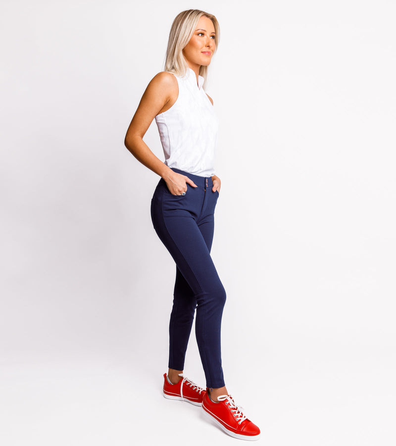 Woman wearing navy pants and a sleeveless white polo.