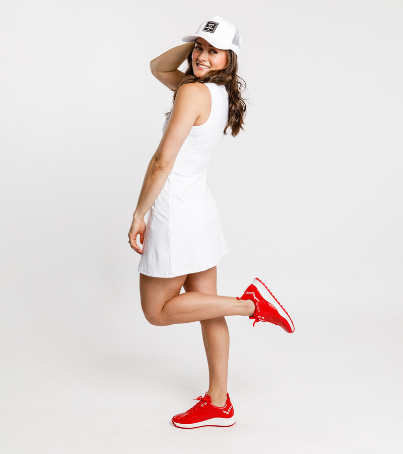 Back view of a woman wearing a sleeveless white dress and Duca del Cosma red golf shoes.