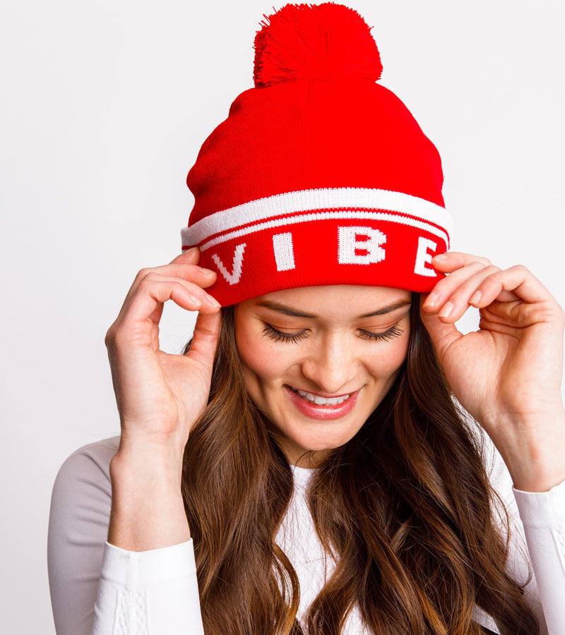 Front view of a woman wearing a red knitted beanie with white graphics that say "BIRDIE VIBES".