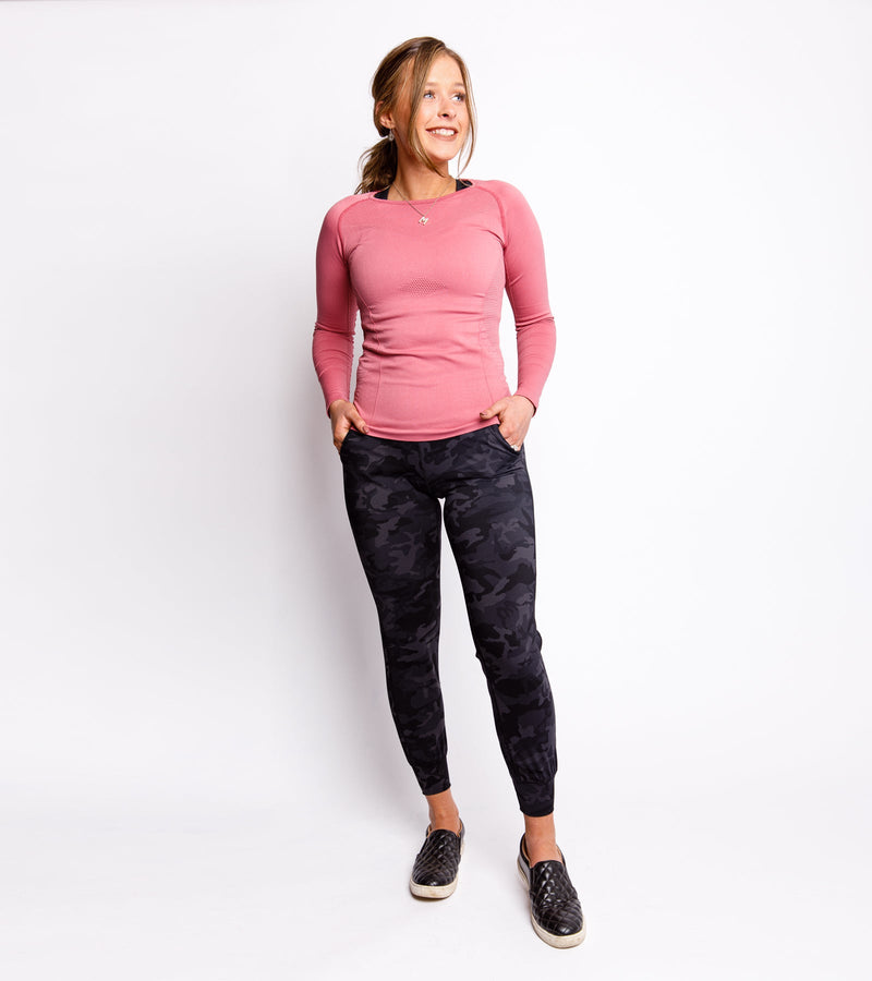 Smiling woman wearing black camo joggers and a long-sleeve pink top.