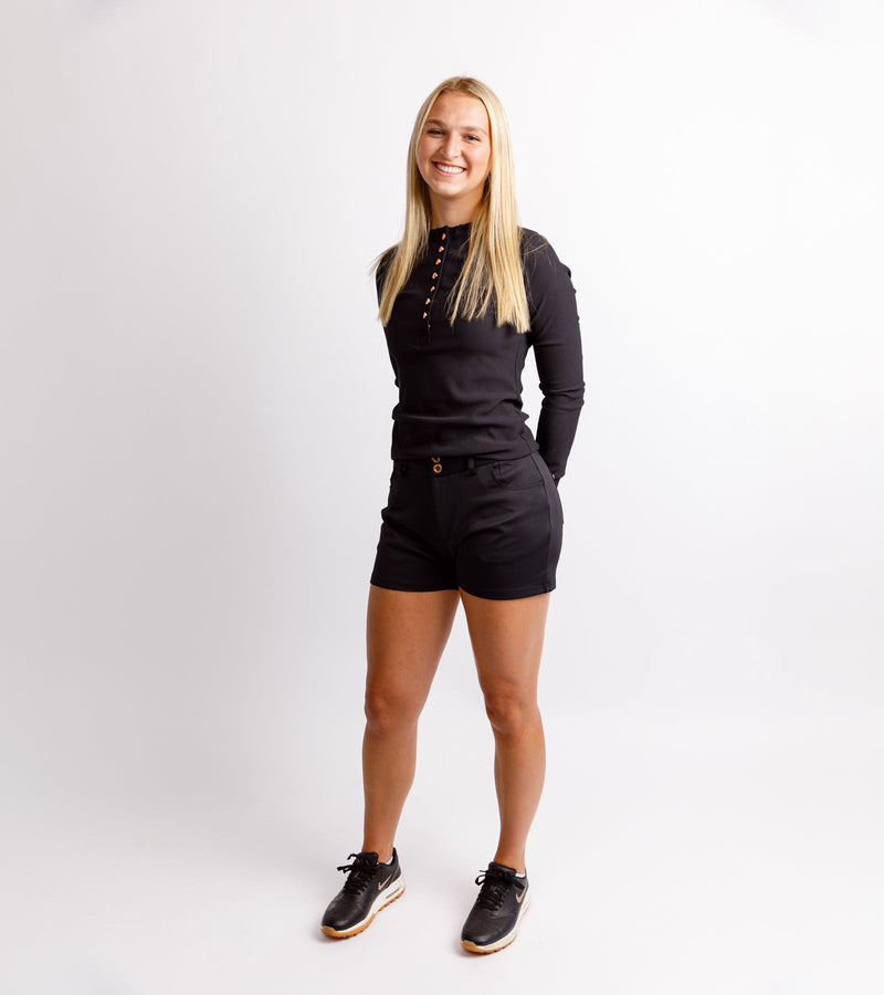 Happy woman wearing a long-sleeve black ribbed shirt with stylish henley rose gold buttons down and black shorts.