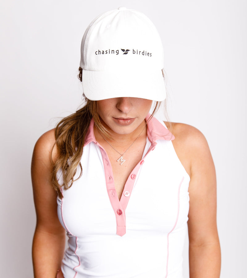 Woman wearing a white dad hat with a black graphic saying "Chasing Birdies" and a sleeveless white top.