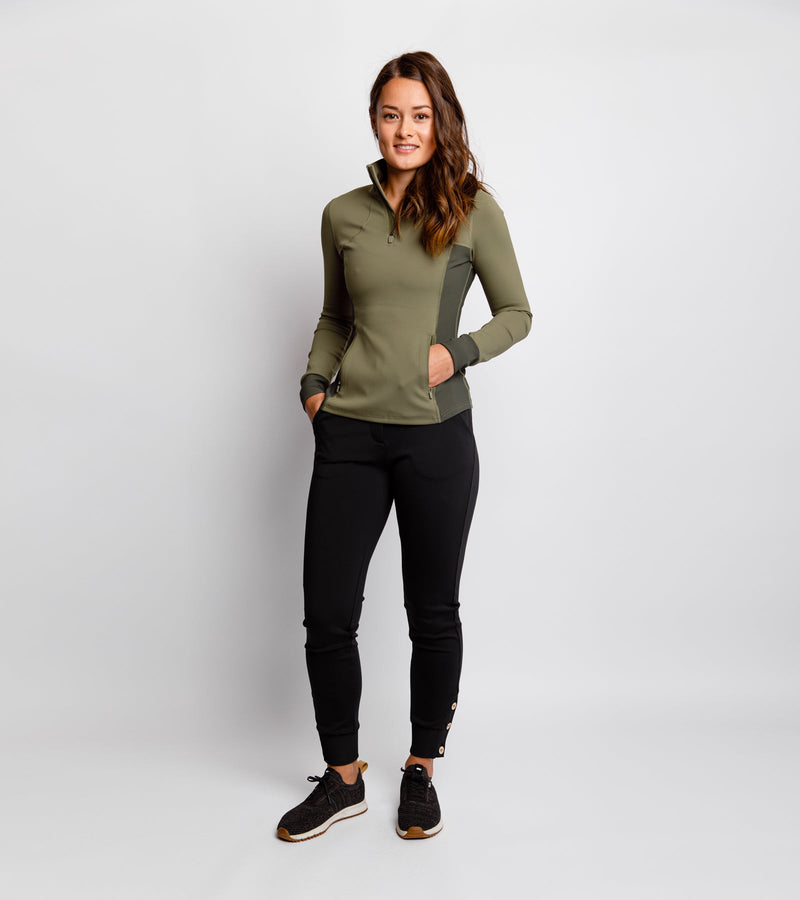 Woman wearing black joggers with gold button detail at the bottom cuff and an army green pullover.