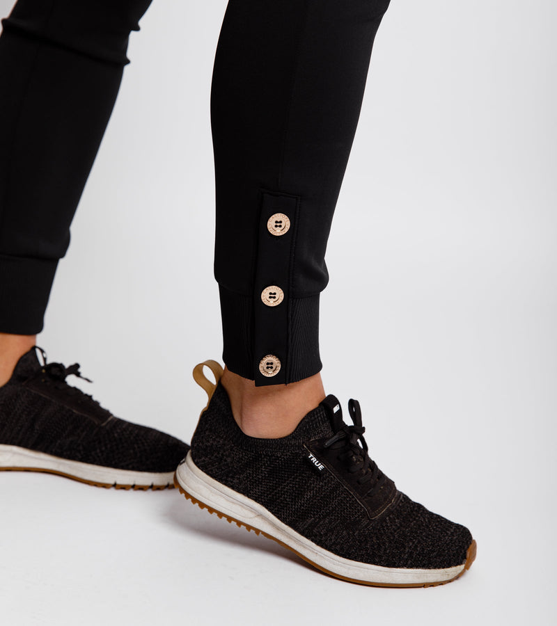 Close-up of the gold button detail at the bottom cuff of a black jogger.