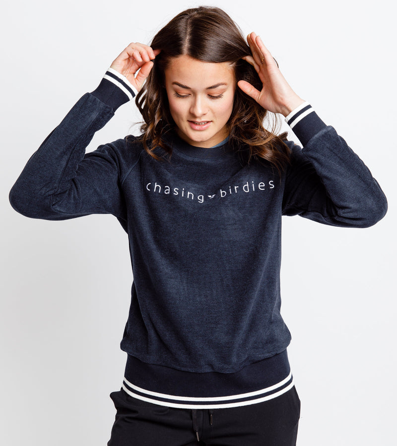 Close-up of a woman wearing a navy sweatshirt with white embroidery across the chest that reads "Chasing Birdies."