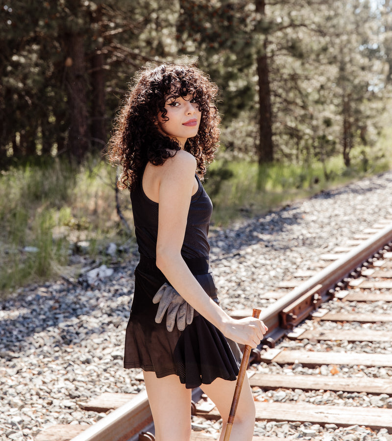 Back view of a woman wearing a racerback black snakeskin polo and a black skirt.