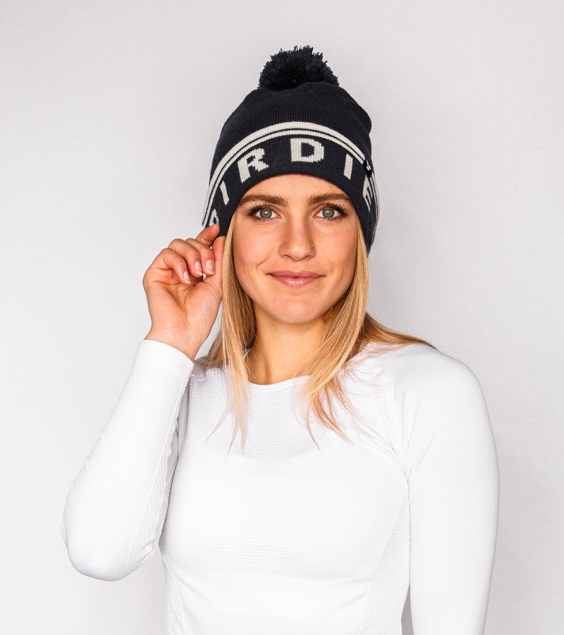 Front view of a woman wearing a navy knitted beanie with white graphics that say "BIRDIE VIBES".