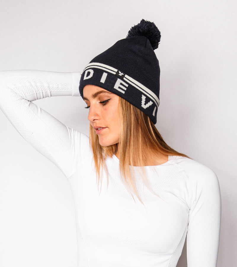 Left view of a woman wearing a navy knitted beanie with white graphics that say "BIRDIE VIBES".