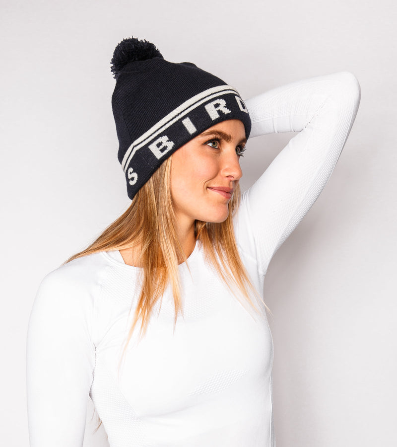 Right view of a woman wearing a navy knitted beanie with white graphics that say "BIRDIE VIBES".