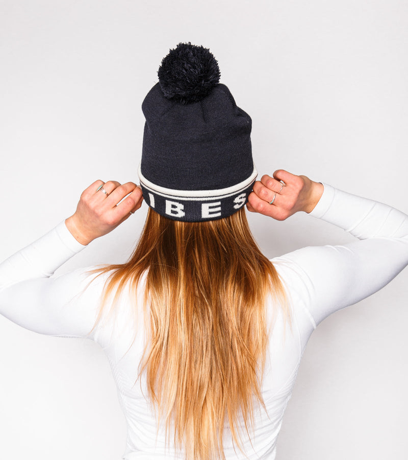 Back view of a woman wearing a navy knitted beanie with white graphics that say "BIRDIE VIBES".