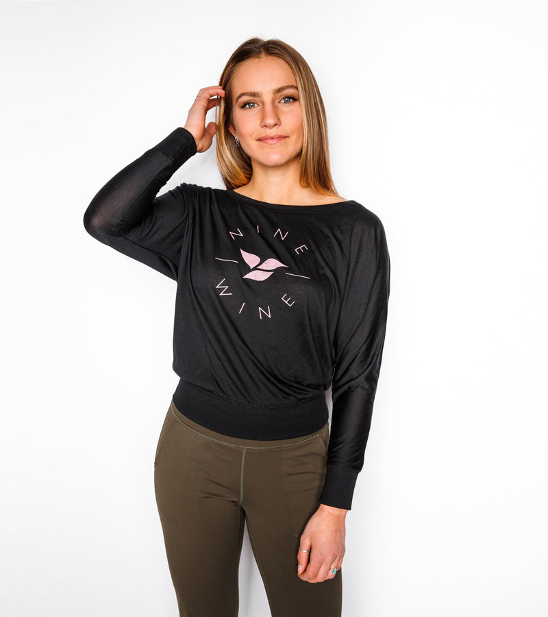 Woman wearing a long-sleeve black slouchy with pink graphics saying "NINE AND WINE."