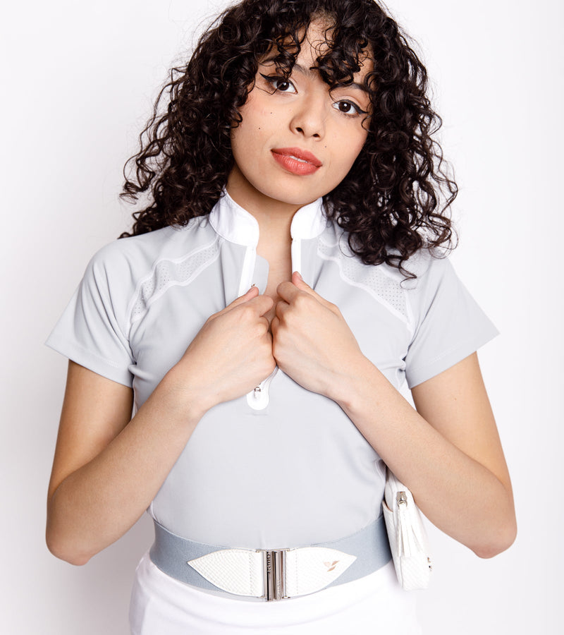 Woman wearing a short-sleeve gray polo with a front bonded zipper with white stitching and a placket. She is also wearing a gray and white belt with a white bag.