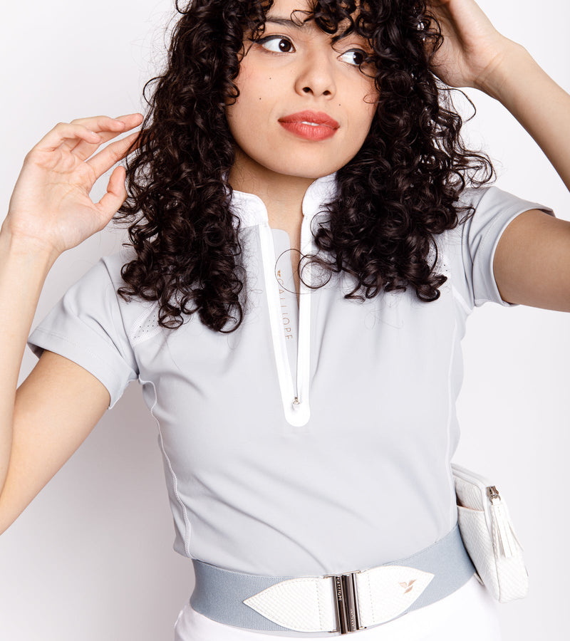 Close-up of a woman wearing a short-sleeve gray polo with a front bonded zipper with white stitching and a placket. She is also wearing a gray and white belt with a white bag.